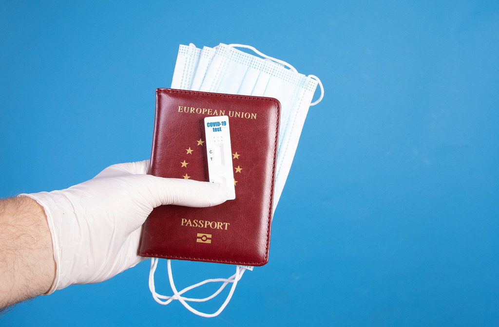 Hand in protective gloves holding passport with face masks and Covid-19 antigen test on blue background Hand in protective gloves holding passport with face masks and Covid-19 antigen test on blue background