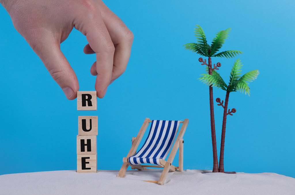 Hand with wooden blocks wiht Ruhe text and beach chair on blue background Hand with wooden blocks wiht Ruhe text and beach chair on blue background