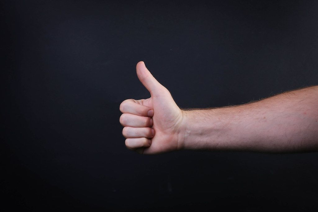 Male hand is showing a thumbs up gesture sign on black background Male hand is showing a thumbs up gesture sign on black background
