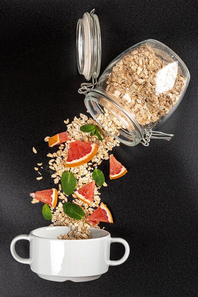 Oatmeal poured from a glass jar with pieces of grapefruit and mint on a dark background with a bowl Oatmeal poured from a glass jar with pieces of grapefruit and mint on a dark background with a bowl