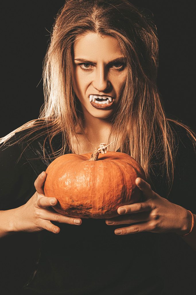 Orange pumpkin in the hands of a vampire woman on dark Orange pumpkin in the hands of a vampire woman on dark