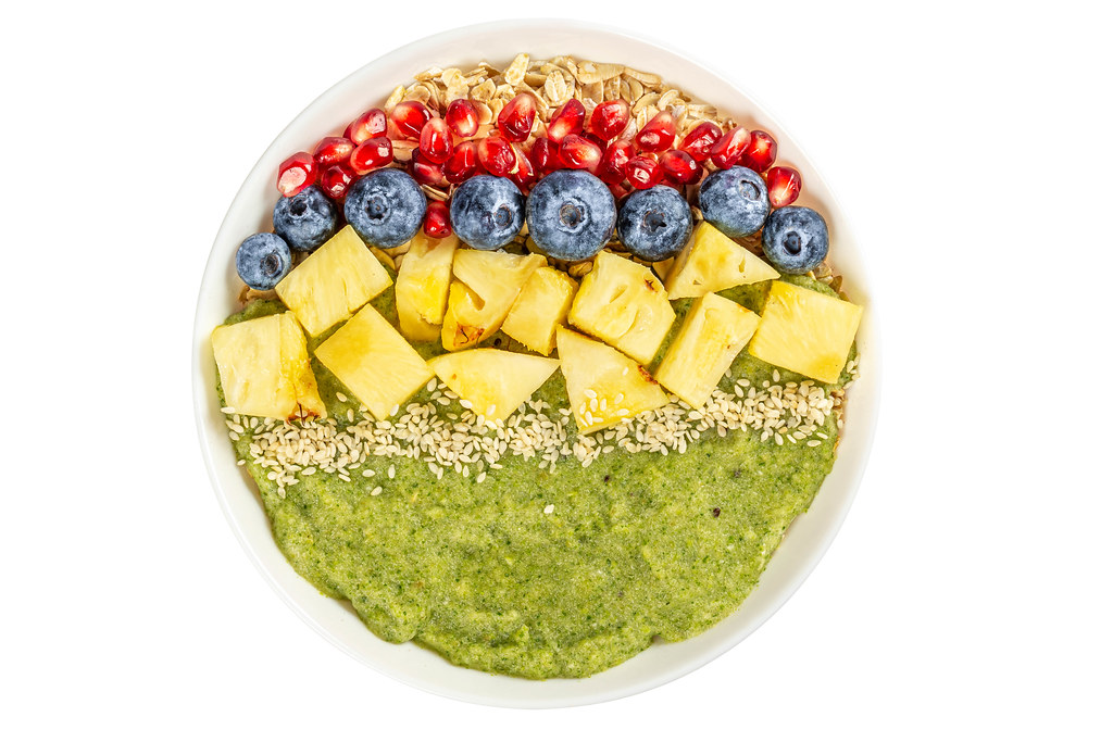 Porridge with blueberries, pomegranate, pineapple pieces, sesame seeds and green fruit puree on white, top view Porridge with blueberries, pomegranate, pineapple pieces, sesame seeds and green fruit puree on white, top view