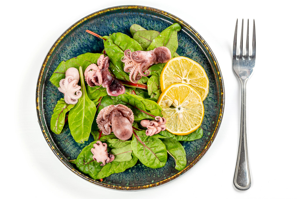 Salad with pickled octopus and green beet leaves on white, top view Salad with pickled octopus and green beet leaves on white, top view