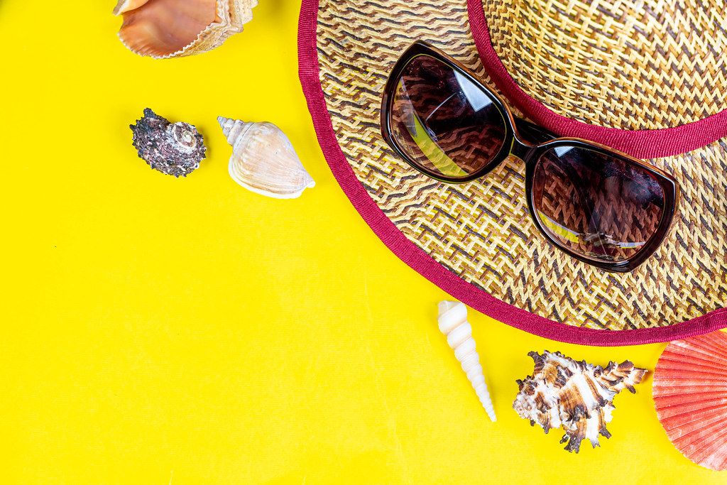 Summer vacation concept. Hat, sunglasses and shells on a yellow background with free space Summer vacation concept. Hat, sunglasses and shells on a yellow background with free space