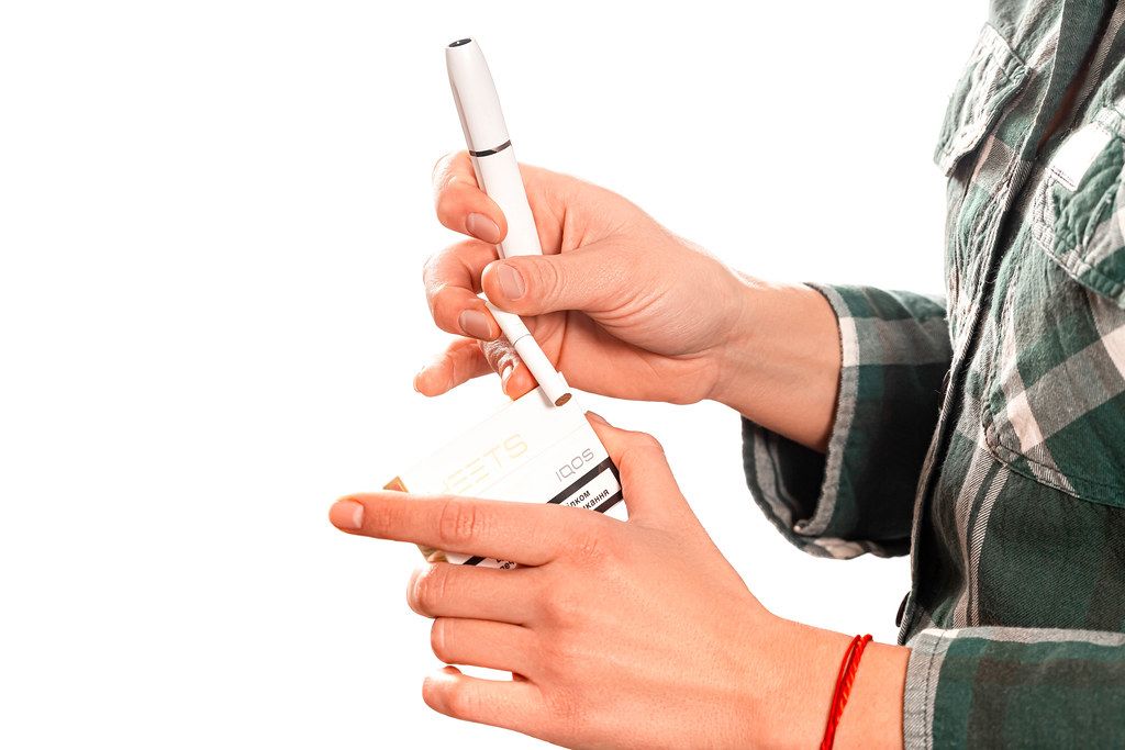 The girl holds in her hand a heating electronic cigarette with a tobacco stick for smoking The girl holds in her hand a heating electronic cigarette with a tobacco stick for smoking