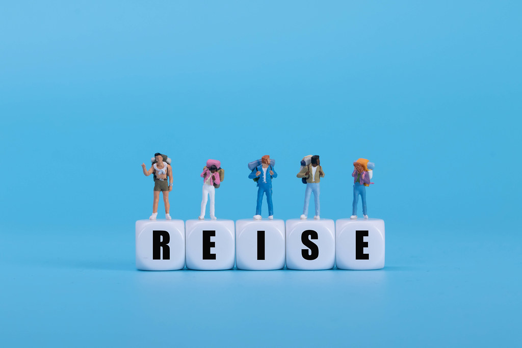 Travelers standing on white blocks with Reise text on blue background Travelers standing on white blocks with Reise text on blue background