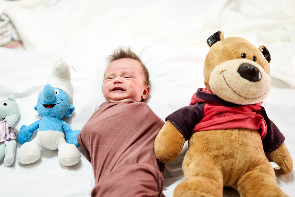 Unhappy baby boy lying between plush toys Unhappy baby boy lying between plush toys
