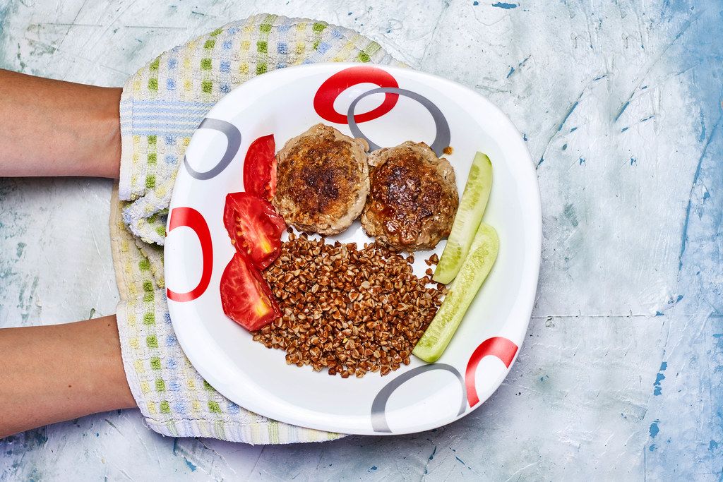 Woman holding a plate of buckwheat and meat cutlets with fresh vegetables Woman holding a plate of buckwheat and meat cutlets with fresh vegetables