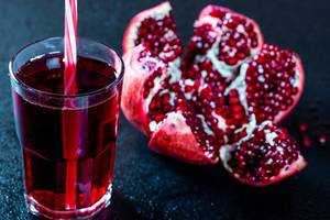 A glass of pomegranate juice with fresh pomegranate on a dark background A glass of pomegranate juice with fresh pomegranate on a dark background