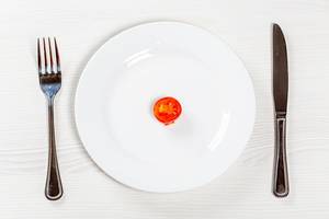 A piece of tomato on a white plate with a knife and fork. Weight loss concept A piece of tomato on a white plate with a knife and fork. Weight loss concept