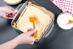 A woman spreads the dough in a baking tray with a kitchen spatula A woman spreads the dough in a baking tray with a kitchen spatula