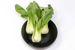 Baby Pak Choi auf schwarzem Teller auf weißem Hintergrund Baby Pak Choi auf schwarzem Teller auf weißem Hintergrund