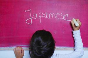 Child writes Japanese word on chalkboard, learning foreign language Child writes Japanese word on chalkboard, learning foreign language