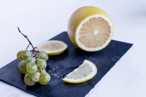 Composition of green grapes and lemon on black board Composition of green grapes and lemon on black board