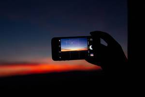 Hand taking photo of a pink sunset with a phone Hand taking photo of a pink sunset with a phone