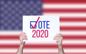 Hands holding board with Vote 2020 concept with USA flag background.jpg Hands holding board with Vote 2020 concept with USA flag background.jpg