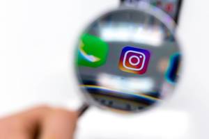 Instagram app on mobile phone photographed through magnifying glass against white background Instagram app on mobile phone photographed through magnifying glass against white background
