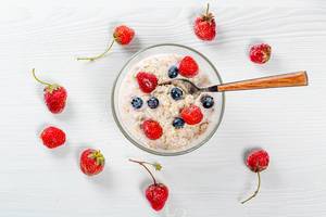 Oatmeal with blueberries and strawberries with spoon on white wooden background. Top view Oatmeal with blueberries and strawberries with spoon on white wooden background. Top view