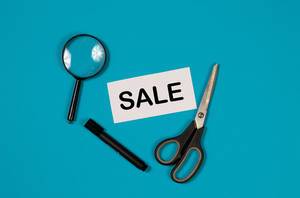 Paper with word Sale and scissors on blue background Paper with word Sale and scissors on blue background