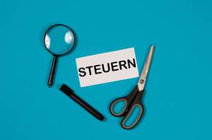 Paper with word Steuern and scissors on blue background Paper with word Steuern and scissors on blue background