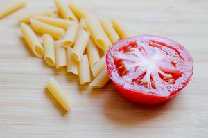 Raw pasta and a tomato on wooden background, kitchen Raw pasta and a tomato on wooden background, kitchen