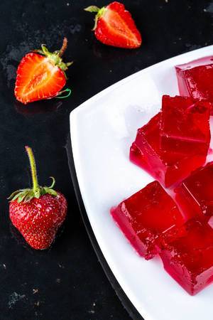 Red jelly cubes with fresh strawberries on a dark background Red jelly cubes with fresh strawberries on a dark background