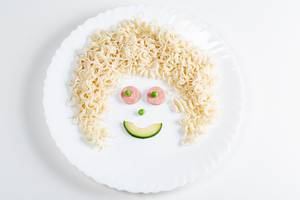 Smiling face made of macaroni, sausage, avocado slice and green peas Smiling face made of macaroni, sausage, avocado slice and green peas