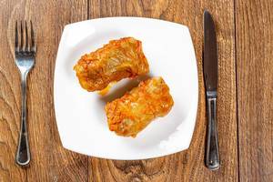 Stuffed stewed in tomato sauce with knife and fork on wooden brown background Stuffed stewed in tomato sauce with knife and fork on wooden brown background