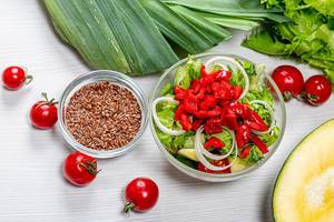 Top view dietary vegetable salad in glass bowl with ingredients on white wooden background Top view dietary vegetable salad in glass bowl with ingredients on white wooden background