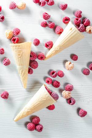 Top view of waffle cone with frozen raspberry berries on white wooden background Top view of waffle cone with frozen raspberry berries on white wooden background