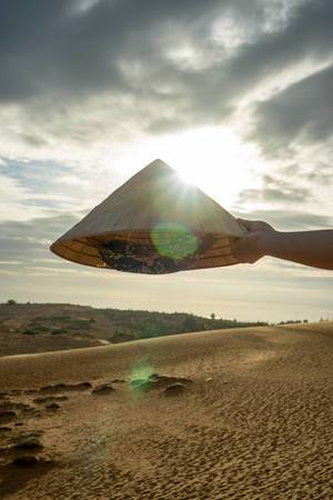 Traditioneller vietnamesischer Dreieckshut vor dem Sonnenuntergang über den roten Sanddünen in Mui Ne, Vietnam Traditioneller vietnamesischer Dreieckshut vor dem Sonnenuntergang über den roten Sanddünen in Mui Ne, Vietnam